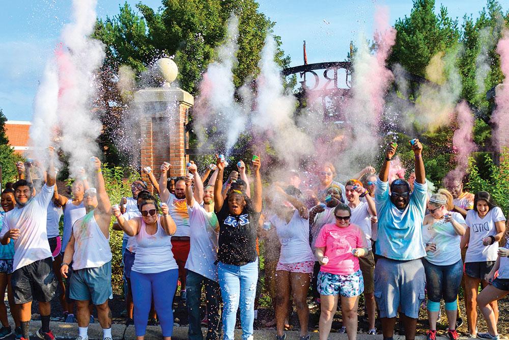 A large group of Greek Life students throw multi-colored dust into the air